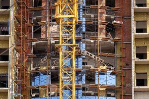 Fragment of an unfinished concrete and brick building under construction with scaffolding and a crane. photo