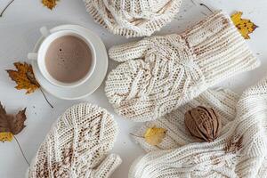 White knitted gloves, hot chocolate, and hat on table in minimalist flat lay, cozy winter scene. photo
