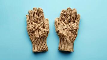 Top view closeup of light brown knitted woolen gloves on blue backdrop. Winter handwear detail photo