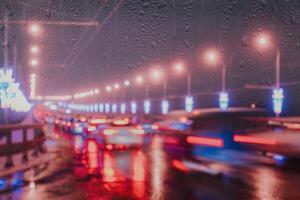 Blurry lights of moving cars and lanterns reflecting on the wet asphalt in the night city behind rain-covered window. photo
