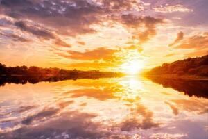 Sunset on the river at summer evening with clouds and trees. Water reflection of a sky. photo
