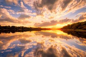 Sunset on the river at summer evening with clouds and trees. Water reflection of a sky. photo