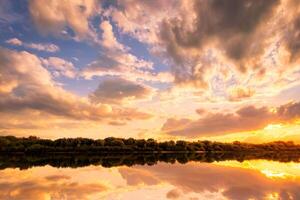 Sunset on the river at summer evening with clouds and trees. Water reflection of a sky. photo
