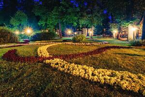 A night park lit by lanterns with a stone pavement, trees, fallen leaves and benches in early autumn. photo
