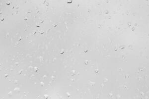 Rain drops on window glasses surface with gray sky background. Natural backdrop of raindrops. The concept of bad rainy weather. photo