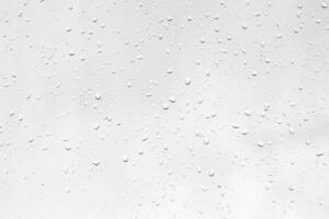 Rain drops on window glasses surface with gray sky background. Natural backdrop of raindrops. The concept of bad rainy weather. photo