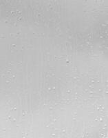 Rain drops on window glasses surface with gray sky background. Natural backdrop of raindrops. The concept of bad rainy weather. photo