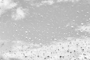 Rain drops on window glasses surface with gray sky background. Natural backdrop of raindrops. The concept of bad rainy weather. photo