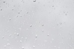 Rain drops on window glasses surface with gray sky background. Natural backdrop of raindrops. The concept of bad rainy weather. photo