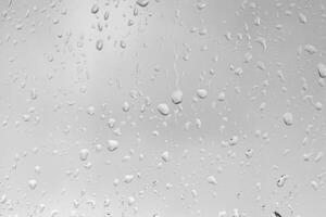 Rain drops on window glasses surface with gray sky background. Natural backdrop of raindrops. The concept of bad rainy weather. photo