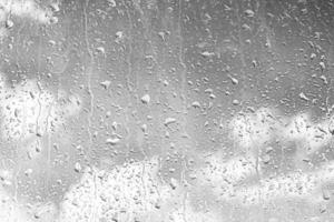 Rain drops on window glasses surface with gray sky background. Natural backdrop of raindrops. The concept of bad rainy weather. photo