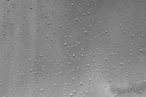 Rain drops on window glasses surface with gray sky background. Natural backdrop of raindrops. The concept of bad rainy weather. photo