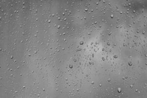 Rain drops on window glasses surface with gray sky background. Natural backdrop of raindrops. The concept of bad rainy weather. photo