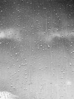 Rain drops on window glasses surface with gray sky background. Natural backdrop of raindrops. The concept of bad rainy weather. photo