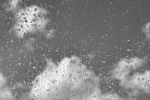 Rain drops on window glasses surface with gray sky background. Natural backdrop of raindrops. The concept of bad rainy weather. photo