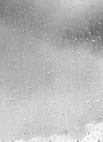 Rain drops on window glasses surface with gray sky background. Natural backdrop of raindrops. The concept of bad rainy weather. photo