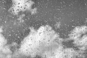 Rain drops on window glasses surface with gray sky background. Natural backdrop of raindrops. The concept of bad rainy weather. photo