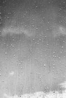 Rain drops on window glasses surface with gray sky background. Natural backdrop of raindrops. The concept of bad rainy weather. photo