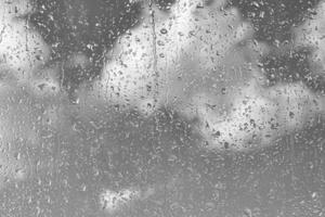 Rain drops on window glasses surface with gray sky background. Natural backdrop of raindrops. The concept of bad rainy weather. photo