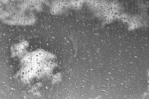 Rain drops on window glasses surface with gray sky background. Natural backdrop of raindrops. The concept of bad rainy weather. photo