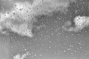 Rain drops on window glasses surface with gray sky background. Natural backdrop of raindrops. The concept of bad rainy weather. photo