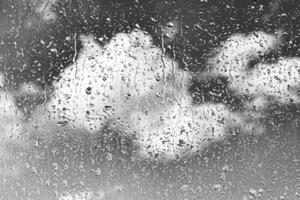 Rain drops on window glasses surface with gray sky background. Natural backdrop of raindrops. The concept of bad rainy weather. photo