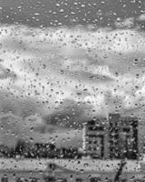 Rain drops on window glasses surface with gray sky and buildinhs background. The concept of bad rainy weather. photo