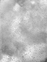 Rain drops on window glasses surface with gray sky background. Natural backdrop of raindrops. The concept of bad rainy weather. photo
