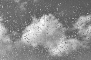 Rain drops on window glasses surface with gray sky background. Natural backdrop of raindrops. The concept of bad rainy weather. photo
