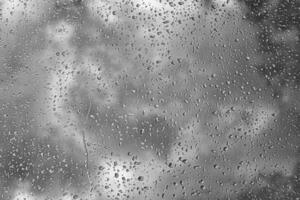 Rain drops on window glasses surface with gray sky background. Natural backdrop of raindrops. The concept of bad rainy weather. photo