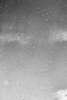 Rain drops on window glasses surface with gray sky background. Natural backdrop of raindrops. The concept of bad rainy weather. photo