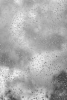 Rain drops on window glasses surface with gray sky background. Natural backdrop of raindrops. The concept of bad rainy weather. photo