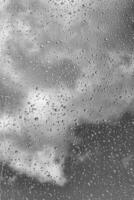 Rain drops on window glasses surface with gray sky background. Natural backdrop of raindrops. The concept of bad rainy weather. photo