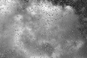 Rain drops on window glasses surface with gray sky background. Natural backdrop of raindrops. The concept of bad rainy weather. photo