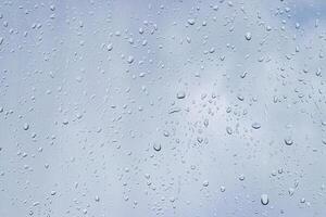 Rain drops on window glasses surface with gray sky background. Natural backdrop of raindrops. The concept of bad rainy weather. photo