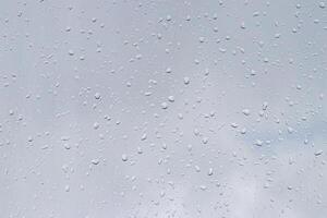Rain drops on window glasses surface with gray sky background. Natural backdrop of raindrops. The concept of bad rainy weather. photo
