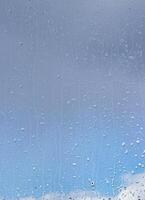 Rain drops on window glasses surface with blue sky and clouds background. Raindrops on a glass. The concept of changing from rainy to sunny weather. photo