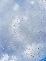 Rain drops on window glasses surface with blue sky and clouds background. Raindrops on a glass. The concept of changing from rainy to sunny weather. photo