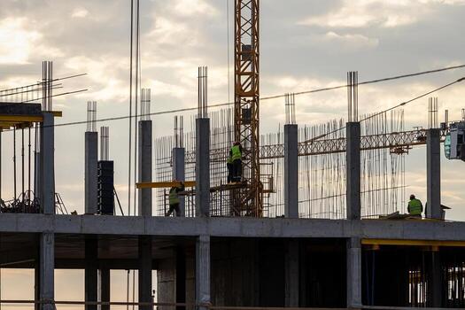 A team of construction workers in and a crane constructing a building on the background of the evening cloudy sky. photo