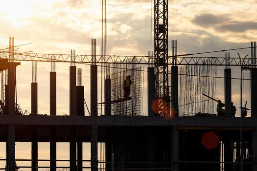 Silhouette of a team of construction workers in and a crane constructing a building on the background of the sunset sky. photo
