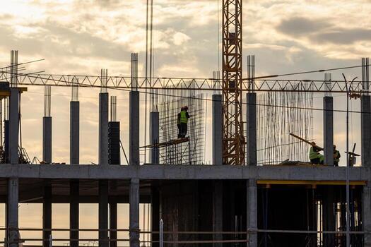 A team of construction workers in and a crane constructing a building on the background of the evening cloudy sky. photo