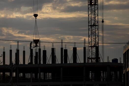Silhouette of a team of construction workers in and a crane constructing a building on the background of the sunset sky. photo