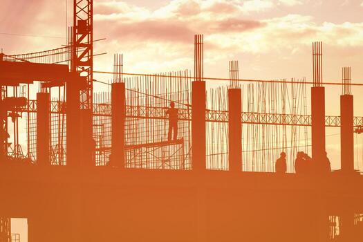 Silhouette of a team of construction workers in and a crane constructing a building on the background of the sunset sky. photo