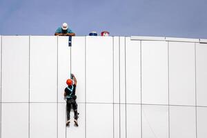 Russia, Kaluga - SEPTEMBER 16, 2020 An industrial climber hanging from a rope with a carabiner and securing the white cladding panels of a building at a construction site. photo