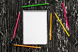 The notebook with squared pages and colorful pencils on a black table with a copy space. photo