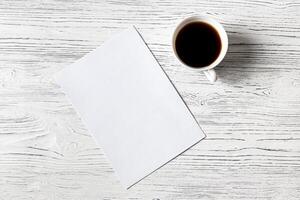 White paper sheet and cup of coffee on a wooden table. Abstract background for design. photo