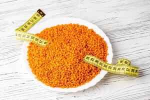 Grains of red lentils and a measuring tape in a plate on a white wooden table. photo