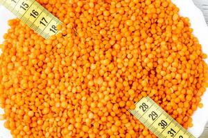 Grains of red lentils and a measuring tape in a plate on a white wooden table. photo