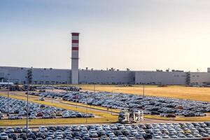 New cars parked in a distribution center on a sunny day in the autumn and car factory buildings with pipes. photo