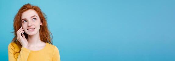 Lifestyle and Technology concept - Portrait of cheerful happy ginger red hair girl with joyful and exciting talking with friend by mobile phone. Isolated on Blue Pastel Background. Copy space photo